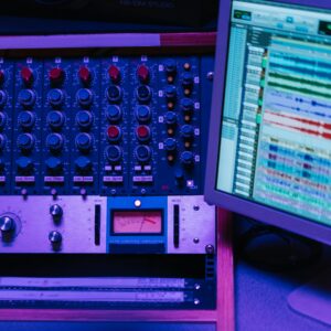 Close-up of a mixing console and screen in a recording studio, showcasing audio editing software.